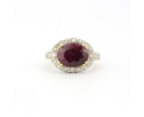 A hallmarked 9ct yellow gold ring set with a large oval cut ruby and diamonds, ruby L. 1.2cm, (O). Two diamonds missing.