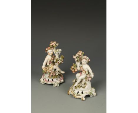 A PAIR OF LATE BOW PUTTI, seated amongst flowers, on a pierced and scroll base, 18th century, one red anchor and dagger mark 