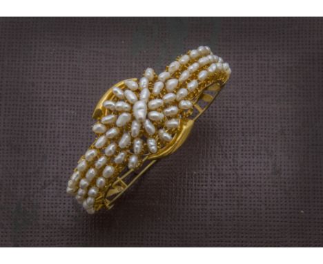 A 1960s Middle Eastern gold and pearl bangle, the front half with three rows of freshwater pearls and centred with a roundal 