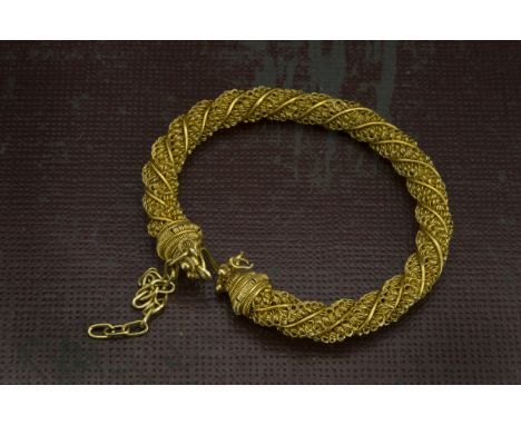 A vintage Middle Eastern yellow metal bangle, the twisted filigree with wire work finials, with safety chain, 33.4g 