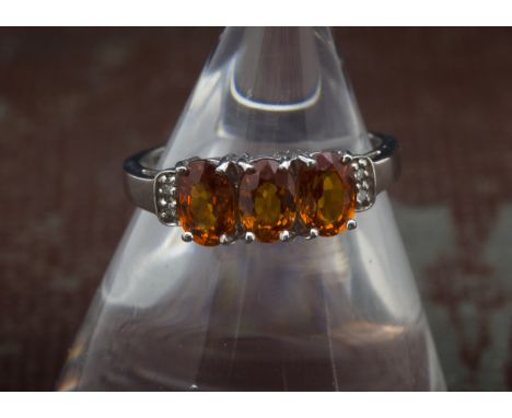 A modern 9ct white gold three stone orange garnet ring, oval probably spessartite stones heightened by two small diamonds to 