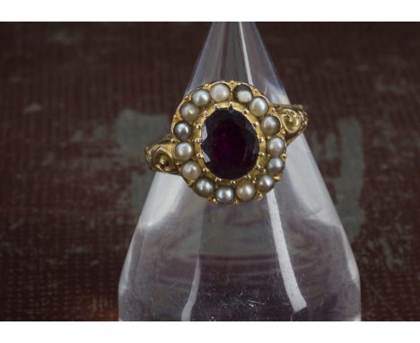 A Victorian gold garnet and seed pearl dress ring, the oval red stone with small white pearl surround, engraved shoulders, un