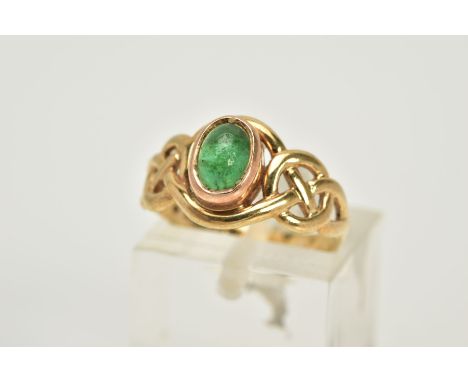 A 9CT GOLD CELTIC RING, designed with a central green stone cabochon assessed as emerald within an openwork Celtic design sur