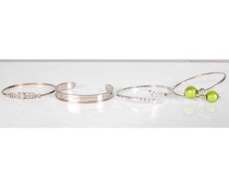 A group of silver bangles to include an open bangle with green glass beads, a hook and eye bangle with pierced geometric pane