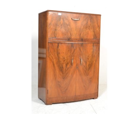 An Art Deco walnut bow fronted cocktail cabinet, the top opening to reveal a glass back fitted interior, over two doors enclo