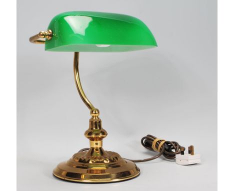 A vintage 20th Century bankers desk lamp having an adjustable green glass shade raised on a brass support and repousse decora