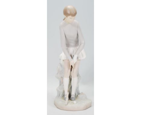 A ceramic Lladro figurine in the form of a lady golfing raised on a naturalistic base. Measures 27cm tall.&nbsp;