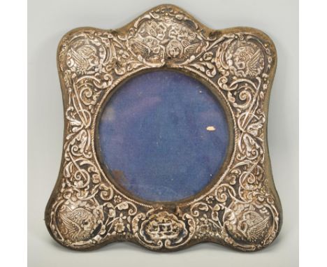 A silver hallmarked rococo easel back picture frame, central circular viewing panel with the frame adorned with cherubs in re