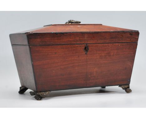 A 19th Century Georgian mahogany tea caddy of sarcophagus form having a brass paw feet and applied floral basket atop with ho