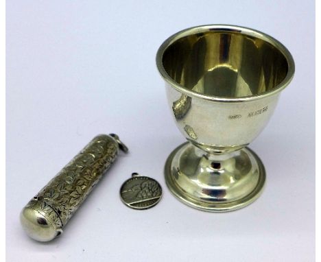 A silver egg cup, a silver cheroot holder case, a silver coin and a pendant