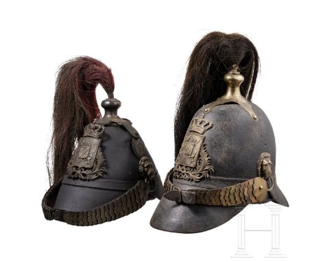 Zwei Helme M 1848 der Landwehrinfanterie Alte Glocke aus derbem schwarzen Leder (geschrumpft), alte gedunkelte Metallbeschläg
