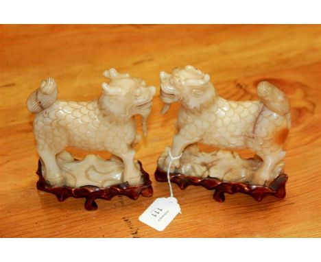 A pair of Chinese carved mutton fat jade kylin, with hooved feet, scaled bodies and bushy tails, raised on carved wood bases,