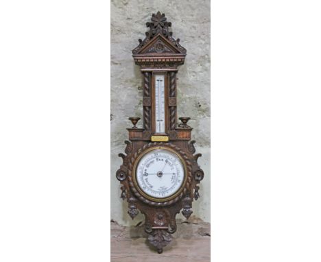 A late Victorian oak aneroid barometer having rope twist and floral carving, turned candle holders and presentation label ins