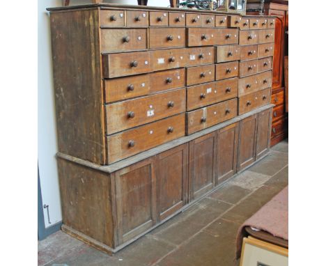 A large oak cabinet, the top section having 36 drawers each with enamel number plate above lower cabinet section, length 299c