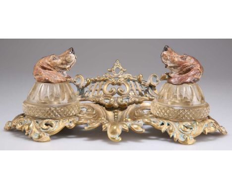 A LATE VICTORIAN BRASS AND COLD-PAINTED INKSTAND each cut-glass inkwell with hounds head cover, (a/f). 28cm wideSlight rockin
