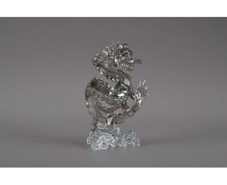 A Swarovski glass dragon sculpture, from the 25 year range, with red glass eyes, on a naturalistic base, 12.5cm high, with re