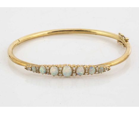 A contemporary gold opal and diamond bangle, the navette shaped setting supporting seven graduated cabochon opals alternately