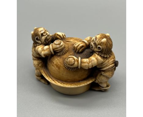 A Japanese Meiji period ivory netsuke, depicting two oni monsters cleaning a sphere. Signed to the base. [4x5.5x4cm] 