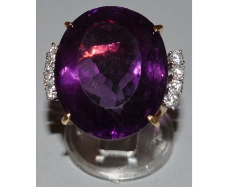 A LARGE AMETHYST OVAL RING with four diamonds to each shoulder, set in yellow gold. 