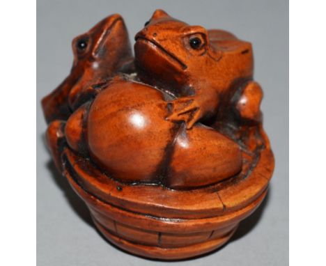 A CARVED WOOD NETSUKE, three toads on a barrel. 