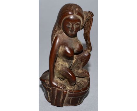 A CARVED WOOD NETSUKE, a nude woman on a barrel. 