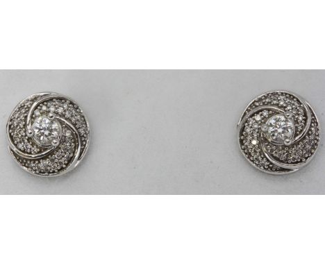 A pair of 18K white gold and diamond stud earrings, the circular-swirl settings centrally set with a RBC diamond and further 