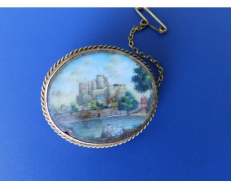 An oval glazed brooch set with a painted panel depicting a castle above a river – '9c', 1.25”.