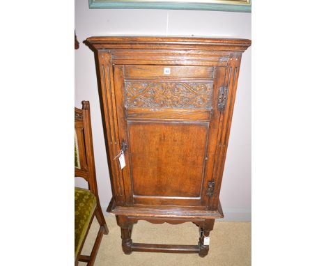 A reproduction oak side cabinet, the carved panel door enclosing central shelf, on stand, possibly Titchmarsh & Goodwin, 137c