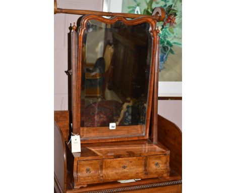 An 18th Century figured walnut toilet mirror, the serpentine crested mirror with bevelled plate, raised on reeded supports, t