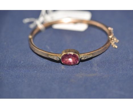 A pink stone and diamond bangle, the oval facet cut pink stone, probably a sapphire, flanked by rose-cut diamonds on a reeded