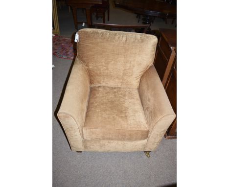 A modern armchair upholstered in light brown velour, raised on mahogany legs terminating in brass castors.