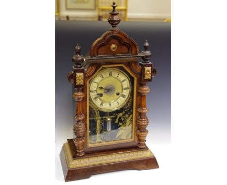 A Junghans walnut mantel alarm clock, turned finials, shaped pediment, enamelled chapter ring, Roman numerals, turned pilaste
