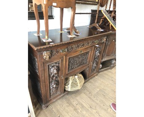 A Victorian carved oak sideboard having upper single drawer with carved devil and goblin heads, central drop down cupboard wi