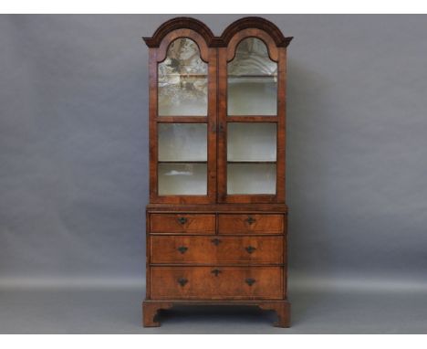 A Queen Anne style walnut bookcase cabinet, the double domed top with glazed doors, over the base, having two short and two l