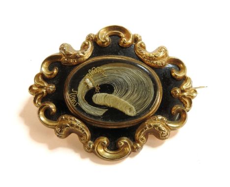 A gold cased black enamel memorial brooch, set with a lock of hair, with engraved inscription verso