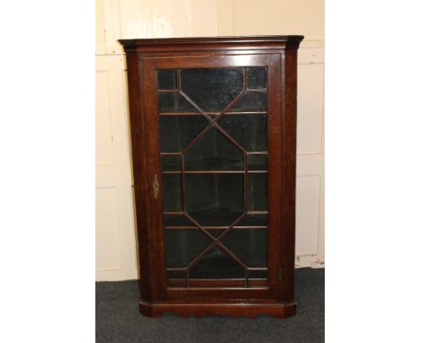 An oak corner cupboard with single glazed panel door enclosing three shelves, on shaped bracket base, 73cm