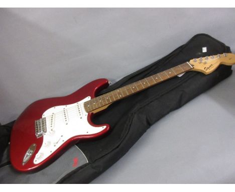 Squire Stratocaster three pick up electric guitar finished in red metallic in a soft case (tremolo arm lacking) together with