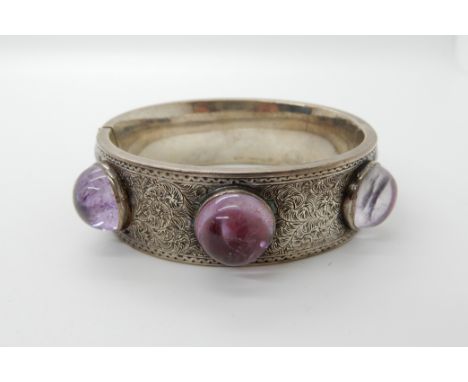 A Victorian white metal wide engraved bangle set with foiled back amethysts, inner diameter 5.6cm x 5.1cm, weight 64.8gms Con