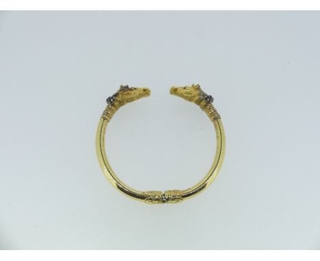 A hinged gold Bangle, with race horse head finials, the bangle with metal core and applied at the hinge with acanthus leaves,