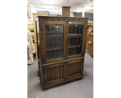 A CARVED OAK DISPLAY CABINET WITH LEADED AND GLAZED DOORS AND LINENFOLD DECORATION 