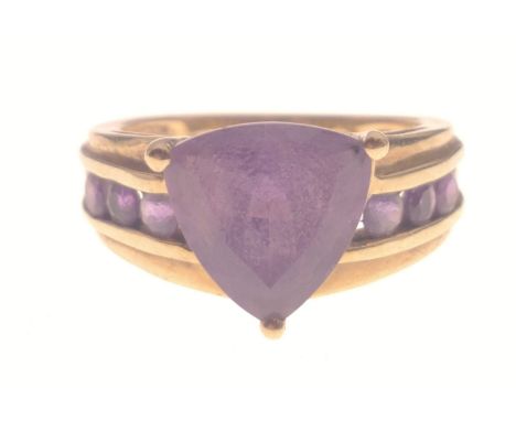 A STUNNING AND SUBSTANTIAL 9K stamped yellow gold ring with a large triangular-cut AMETHYST stone centred flanked by three fu