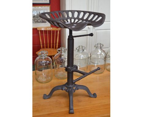A cast iron tractor seat converted to an adjustable swivelling bar stool with rope twist footrest, quatrefoil base, four legs