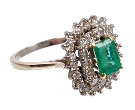 Emerald and diamond cluster ring with a rectangular step cut emerald surrounded by two tiered borders of brilliant cut diamon