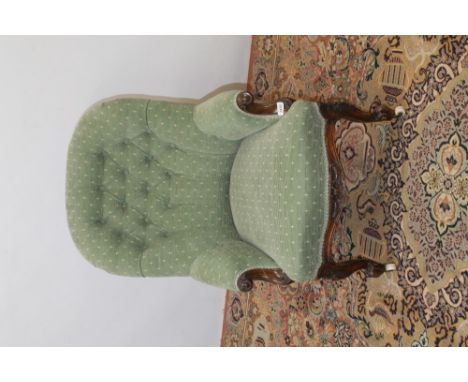 Victorian carved walnut framed button-back armchair with green upholstery, on carved front legs and ceramic castors