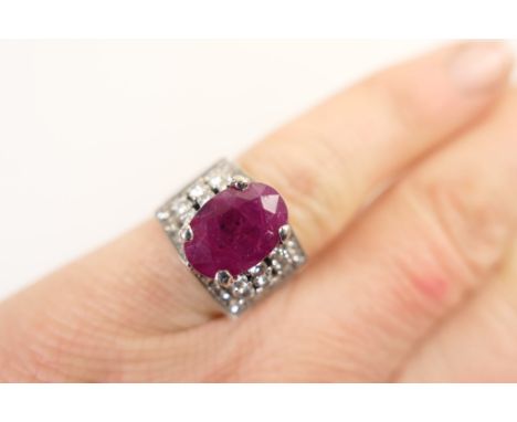 Ruby and diamond cluster ring, the oval ruby approx. 10mm x 7mm, in a raised four claw mount flanked on either side with six 