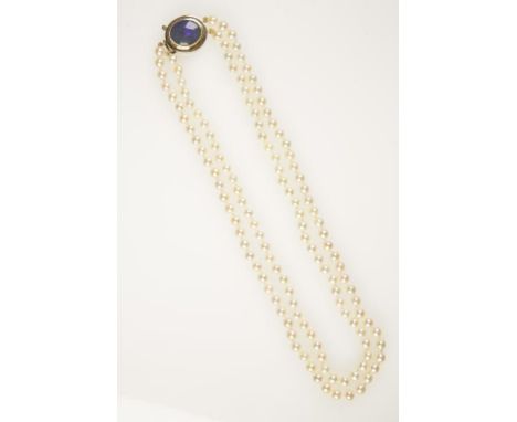 A DOUBLE STRAND CULTURED PEARL NECKLACE, each pearl knotted and terminating in a 9ct yellow gold clasp set with an oval dark 