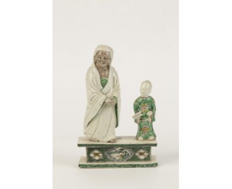 A CHINESE FAMILLE VERTE FIGURE GROUP, modelled as a cloaked louhau and attendant, raised on a pedestal base, Kangxi period, 2