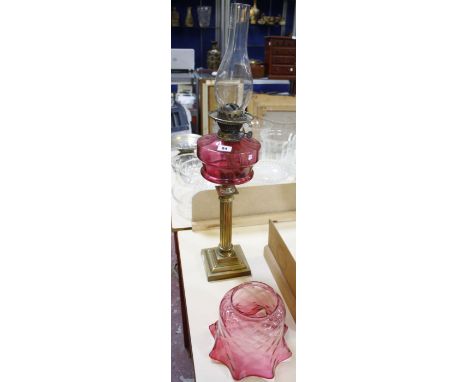 A Victorian oil lamp with cranberry glass shade and reservoir, on a brass reeded column base, 74cm overall height