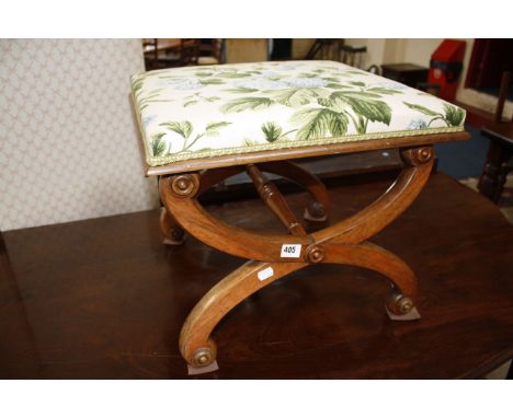 A Victorian X-shaped walnut stool, the sides joined by ring turned stretcher, the padded seat covered in floral patterned clo