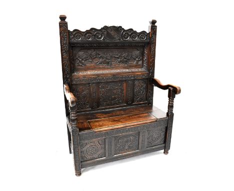 An antique and later carved box seat settle, the back profusely carved with coat of arms and central panel depicting a huntin